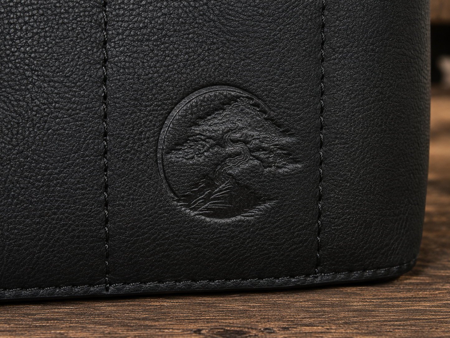 Close-up of a black Bonsai bag, showing a circular embossed logo of a bonsai tree on a wooden surface.