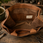 A brown leather Bonsai bag shown open on a rustic wooden workbench, with tools and a bonsai plant around it. A small interior label reads SECHI'S.