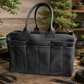 A black leather Bonsai tote bag with dual top handles, set on a rustic wooden table surrounded by bonsai trees, gardening tools, and soil.